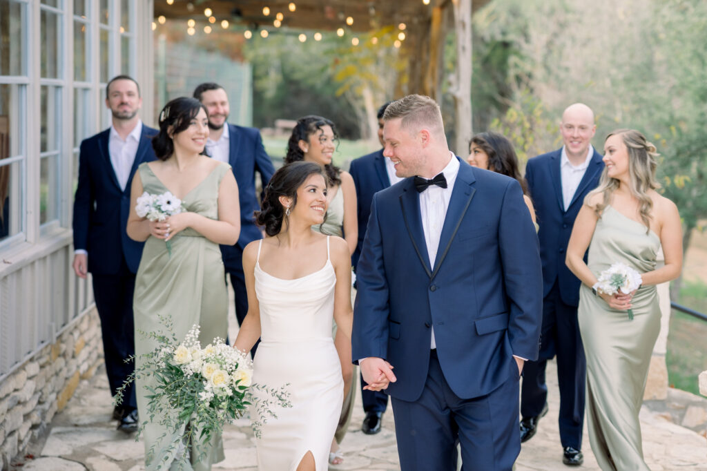 Bridal party walking at Jacob's Well Vineyard in Wimberley, Texas. Bridesmaids are wearing sage green and groomsmen are wearing navy suits.