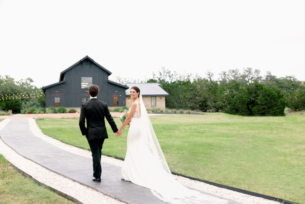 Bride and Groom walking and holding hands as newly weds outside of Morgan Creek Barn in Dripping Springs, Texas.  
