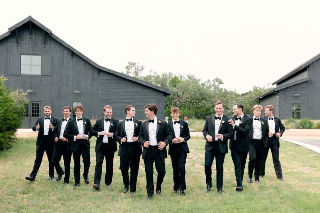 Groomsmen walking and laughing together at Morgan Creek Barn in Dripping Springs, Texas.