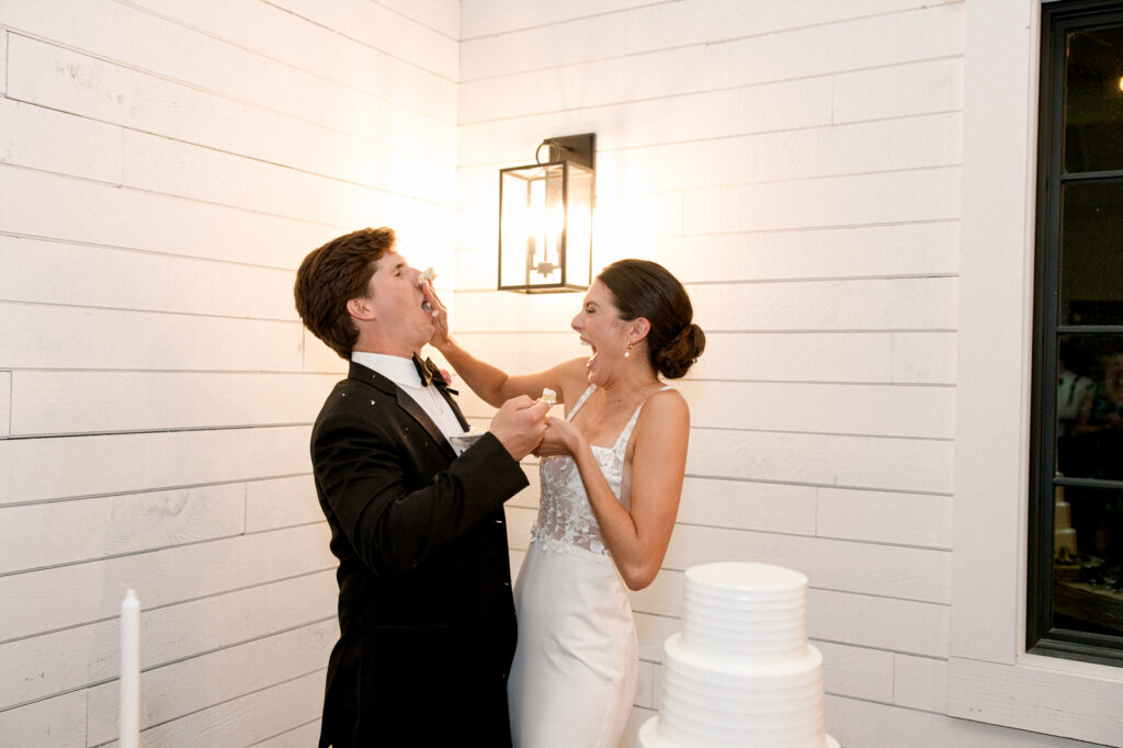 Bride smashing cake in the groom's face in the modern reception hall at Morgan Creek Barn. 