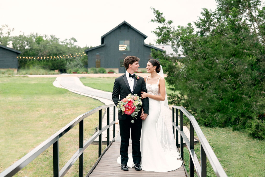 Bride and Groom standing on the bridge outside of Morgan Creek Barn venue in Dripping Springs, Texas. 