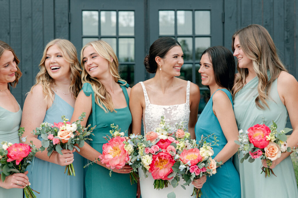 Bridesmaids laughing together in their colorful dresses and beautiful pink blooms at Morgan Creek Barn in Dripping Springs, Texas.