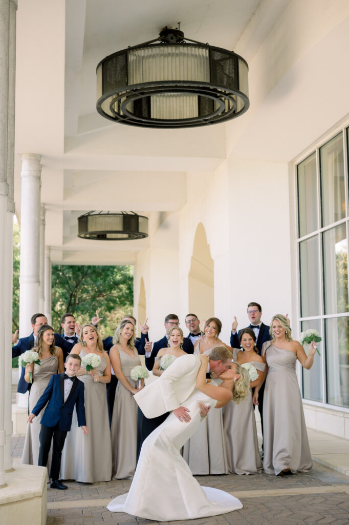 A classy bridal party cheering as bride and groom dip and kiss at San Antonio Wedding Venue.
