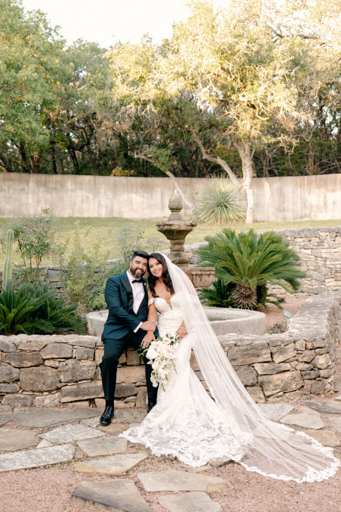 Bride and Groom sitting at the fountain on rock wall at Lost Mission Wedding Venue by Lois M Photography. 