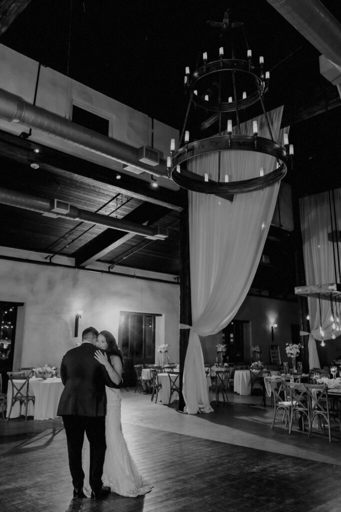 Bride and groom doing their last dance in the reception hall under large chandelier at Lost Mission.