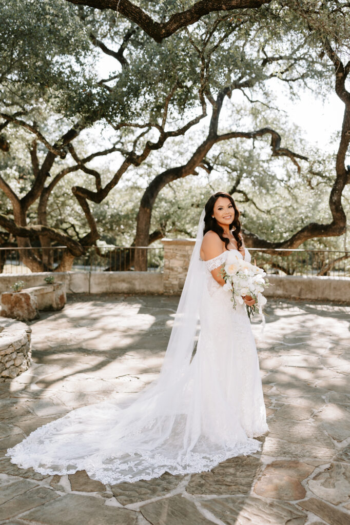 Bride surrounded by oak trees on patio in Spring Branch at the Spanish inpired Lost Mission Wedding Venue. 