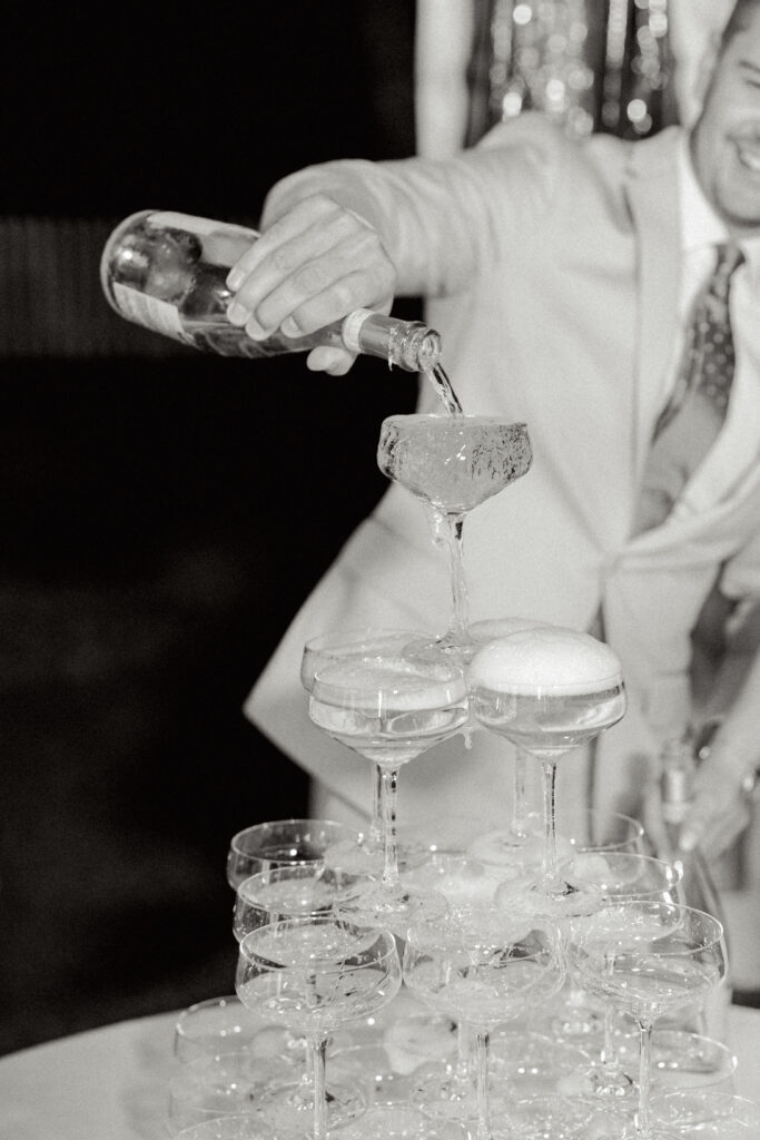 A groom pouring champagne in a champagne tower, a 2024 wedding trend, at wedding in Austin, Texas. 