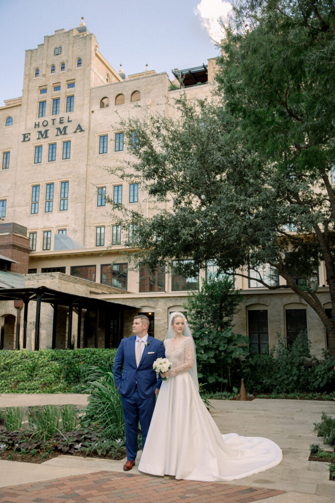 Bride in her timeless elegant weddings dress and groom in his navy suit stand in front of Hotel Emma.