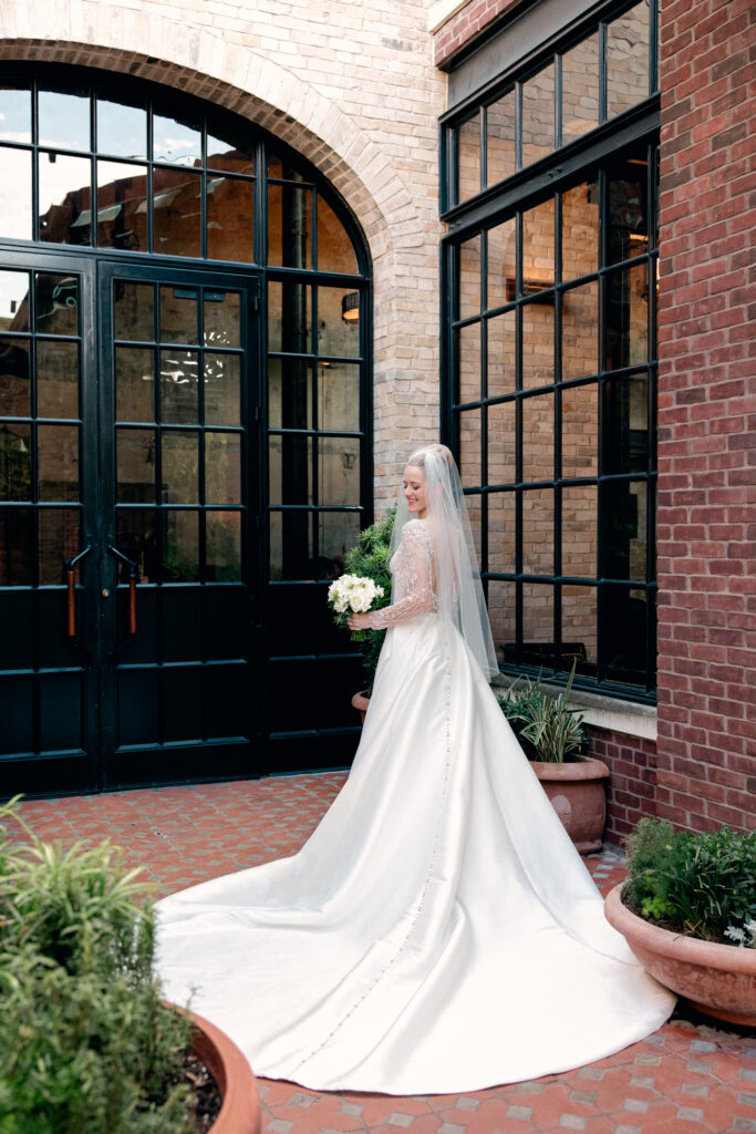 Bride in the front of Hotel Emma with elegant wedding dress and large black doors.