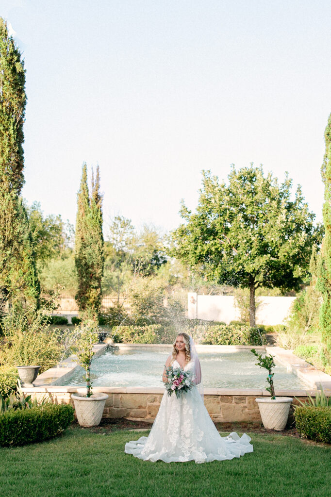 Bride during her bridal session at Thistlewood Manor in front of the expansive fountain surrounded by greenery