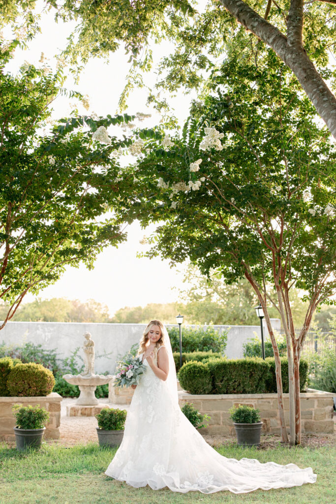Elegant bridal portraits of bride with floral arrangement outside in the Courtyard by the French inspired fountain at Thistlewood Manor and Gardens 