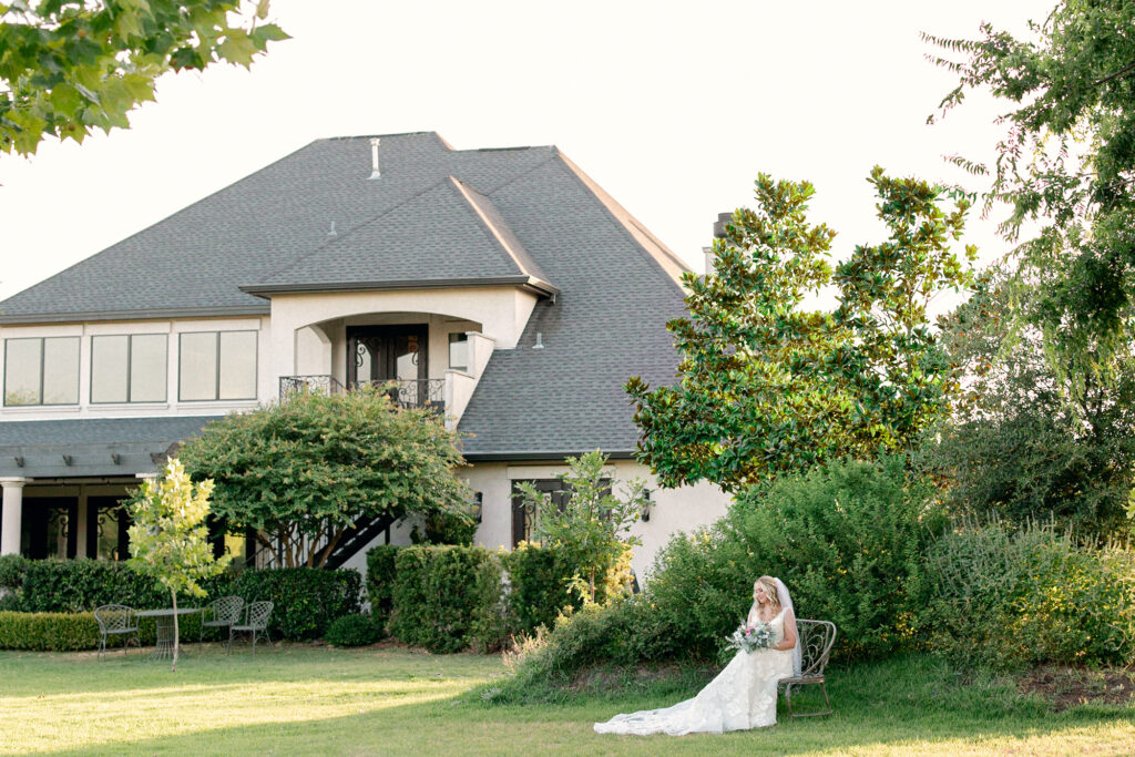 Bride sitting on a bench at Thistlewood Manor and Gardens with the Manor in the background 
