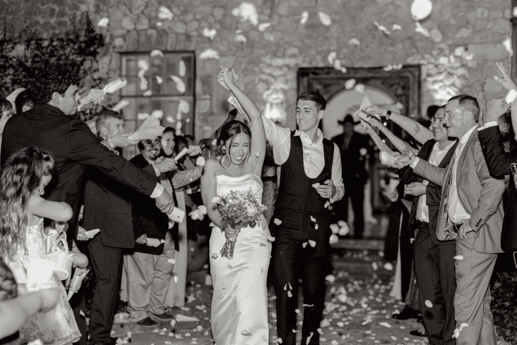 Bride and groom running through flower petals thrown by guests during their send off at the end of their wedding day at the Veranda in San Antonio