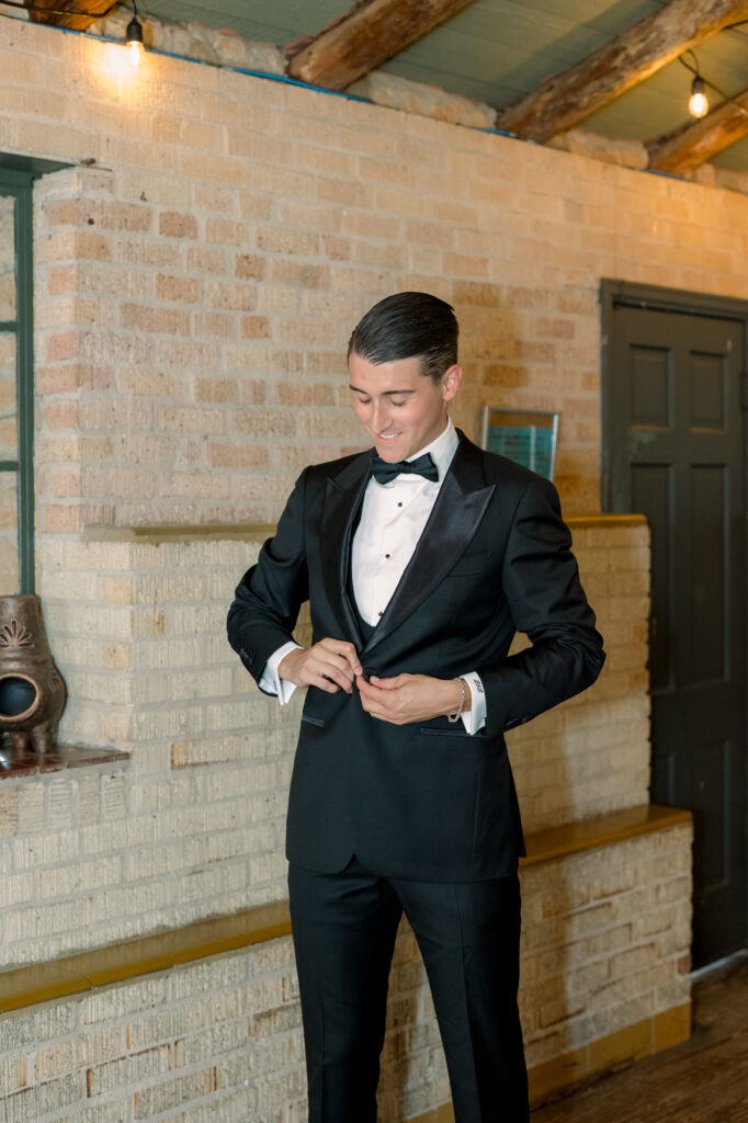 Groom getting ready in groom's suite buttoning his suite 