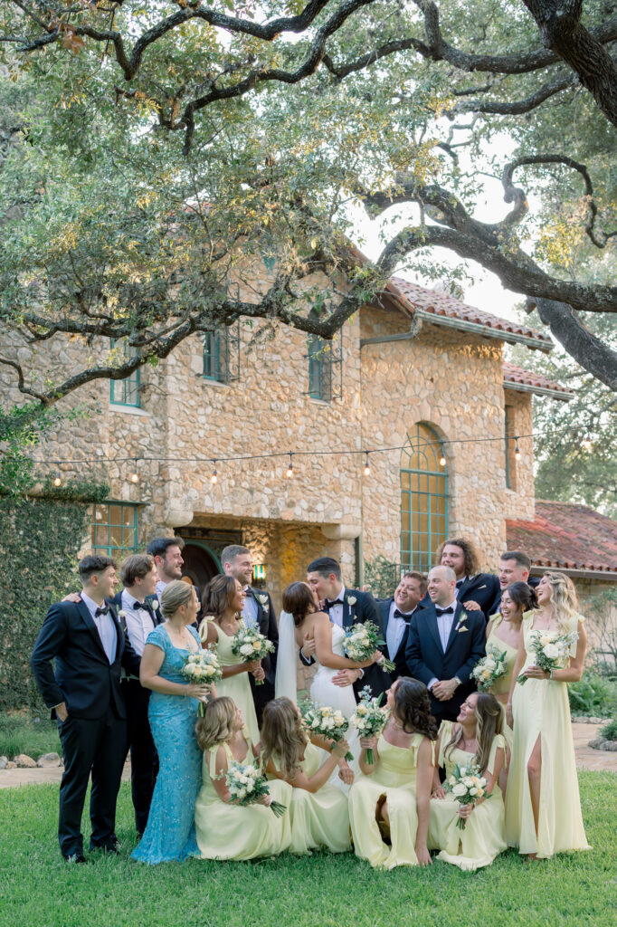 Bridal Party on the lawn in front of the Estate House cheering as the bride and groom kiss at the Veranda in San Antonio, Texas by Lois M Photography