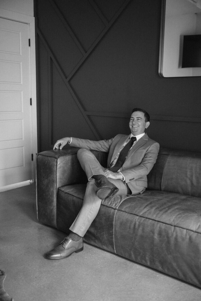 Groom sitting on the couch in the groom's suite at Posey Meadows