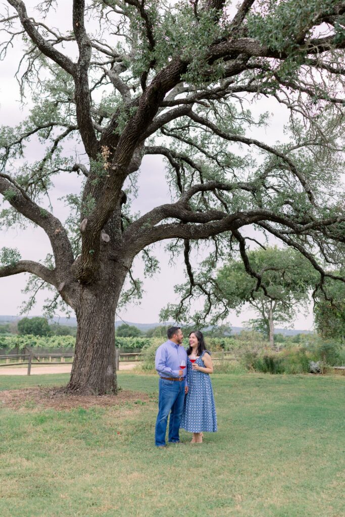 A newly engaged couple posing under a large tree